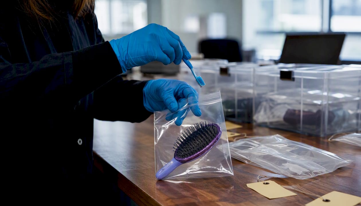 Gloved hands packaging toothbrush and hairbrush for forensic use