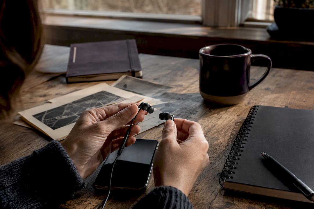 Hands holding earbuds over dark smartphone